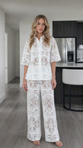 Front view of woman wearing white floral lace button-down shirt and wide-leg pants set
