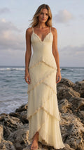Front view of woman wearing yellow embellished tiered maxi dress on coastal rocks